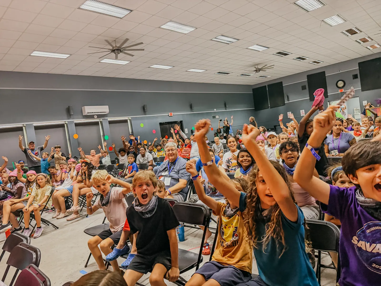 A chapel full of campers cheering with their hands in the air